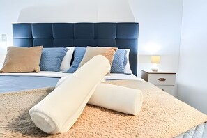 En snyggt bäddad säng med en blå sänggavel, en beige pläd och ett nattduksbord med en lampa.