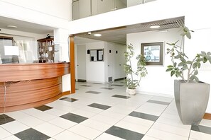 Ett receptionsområde med en bardisk i trä, en stor krukväxt och ett klinkergolv.