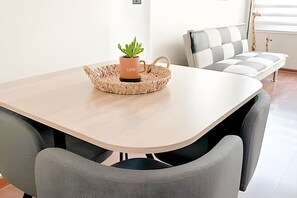 Ett modernt matområde med ett bord i ljusa färger, en vävd bordstablett, en krukväxt och grå stoppade stolar.