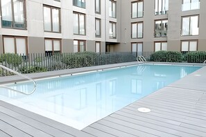 A swimming pool with a wooden deck, surrounded by a fence and a building with multiple windows. - Contemporary, comfortable apartment with WiFi and air conditioning (Santiago)