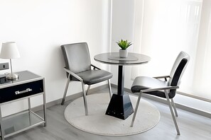 A modern room with a round table, two chairs, a small potted plant, a lamp, and a desk with drawers. - Contemporary, comfortable apartment with WiFi and air conditioning (Santiago)