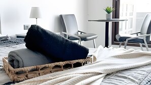 A neatly made bed with a dark blanket and a woven basket, two chairs, a small table with a plant, and a lamp. - Contemporary, comfortable apartment with WiFi and air conditioning (Santiago)