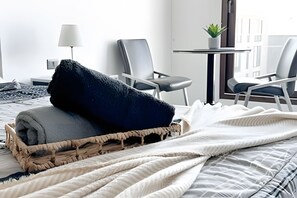 A neatly made bed with a dark blanket and a woven basket, two chairs, a small table with a plant, and a lamp. - Contemporary, comfortable apartment with WiFi and air conditioning (Santiago)
