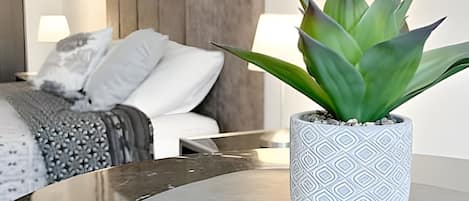 A modern hotel room with a bed, a nightstand, a potted plant, and a round table.