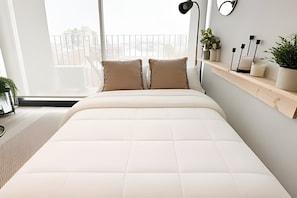 Een moderne slaapkamer met een groot bed, een nachtkastje met een lamp, en uitzicht op de stad door het raam.