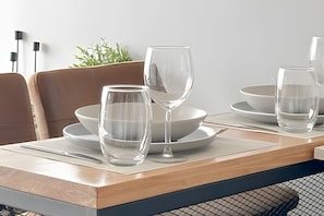 Een eettafel met helder glaswerk en borden, een plantje op de achtergrond, en een moderne stoel.