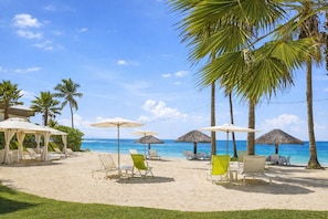 Una playa con palmeras, sillas de descanso y sombrillas.