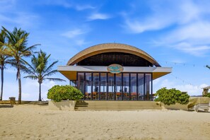 Ein Gebäude direkt am Strand mit einer gewölbten Dachlinie, einem Schild mit der Aufschrift 'Wahaca's Bar' und Sitzgelegenheiten im Freien.
