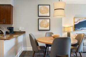 Eine moderne Küche mit integrierter Kaffeemaschine, einem Essbereich mit rundem Tisch und Stühlen, sowie zwei gerahmten Blätter-Kunstwerken an der Wand.