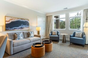 Ein Hotelzimmer mit grauem Sofa, zwei Sesseln, einem Couchtisch und einem Gemälde an der Wand.