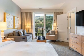 A hotel room with a bed, a sofa, a chair, a desk, a TV, and a balcony with a view of the hills. - Gondola Right Outside - Westin Riverfront 2-Bedroom Villa (Avon)