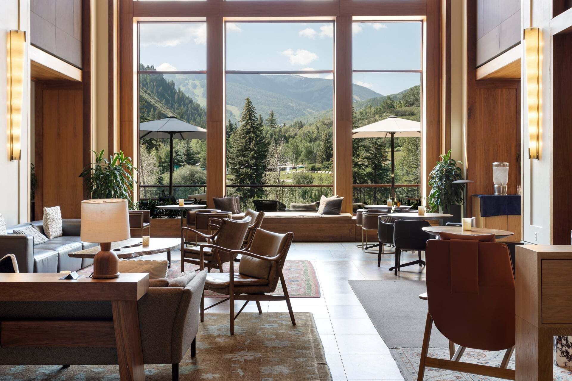 A spacious indoor area with large windows offering a mountain view, furnished with leather chairs and tables, and equipped with a bar area.