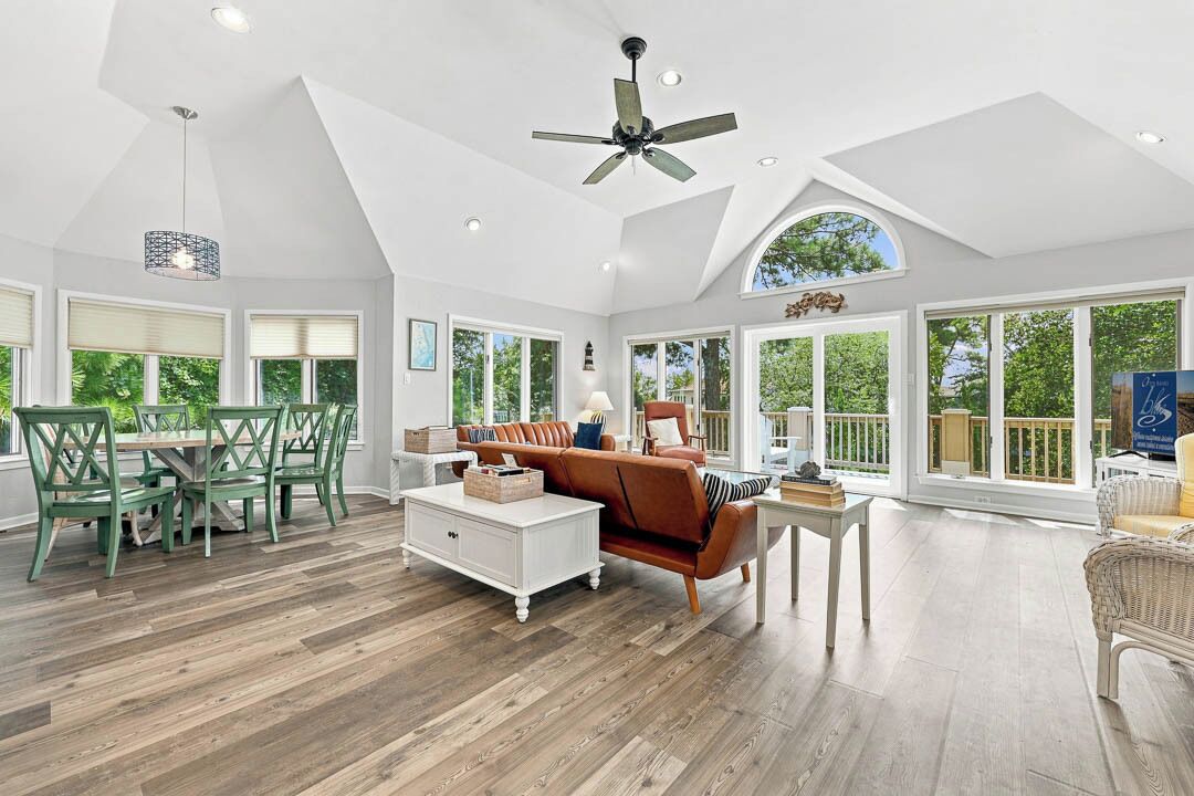 A spacious living room with a high ceiling, a ceiling fan, and large windows offering a view of the outdoors.