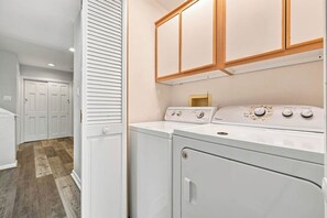 A laundry area with a washer and dryer, wooden cabinets above, and a door leading to a closet. - Ultra Classic | Private Pool, Hot Tub, and Community Pool (Corolla)