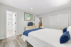 A bedroom with a bed, a dresser, a painting, and a door leading to another room.