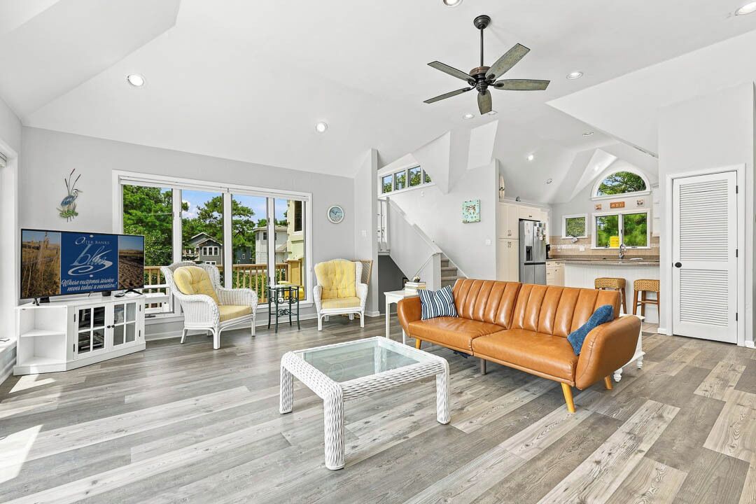 A spacious living room with a large sofa, a coffee table, and a television. There is a staircase leading to an upper level.