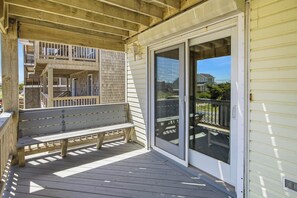 Eine Holzterrasse mit einer Bank, einer Schiebeglastür und Blick auf ein Haus.