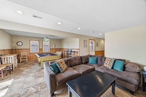 A living room with a brown leather sofa, a pool table, and a dining area with wooden furniture. - Avalon Alibi | 300 ft to the beach | Private Pool, Hot Tub, and Pool Table (Kill Devil Hills)