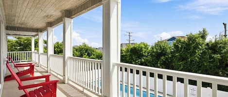 A covered outdoor area with a pool, white railings, and red chairs.