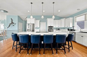 A modern kitchen with white cabinets, a central island with bar stools, and pendant lighting. - Sea To Sound | 740 ft to the beach | Private Pool, Hot Tub, and Dog Friendly (Duck)