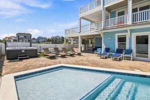 A swimming pool with lounge chairs, a hot tub, and a two-story building with balconies. - Sea To Sound | 740 ft to the beach | Private Pool, Hot Tub, and Dog Friendly (Duck)