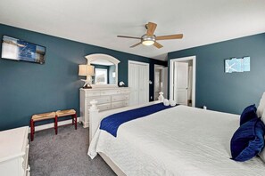 A bedroom with a bed, a dresser, a bench, a ceiling fan, and a door. - Sea To Sound | 740 ft to the beach | Private Pool, Hot Tub, and Dog Friendly (Duck)