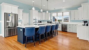 A modern kitchen with white cabinets, stainless steel appliances, and a central island with bar stools. - Sea To Sound | 740 ft to the beach | Private Pool, Hot Tub, and Dog Friendly (Duck)