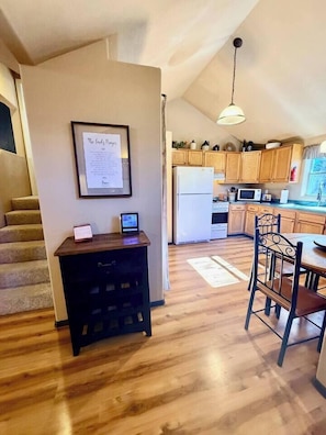A kitchen with wooden cabinets, a refrigerator, and a dining area with a table and chairs. - “Peace of the Mountains” (Cloudcroft)