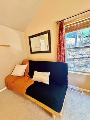 A room with a bed, a window with a view of trees, a mirror on the wall, and a red curtain. - “Peace of the Mountains” (Cloudcroft)