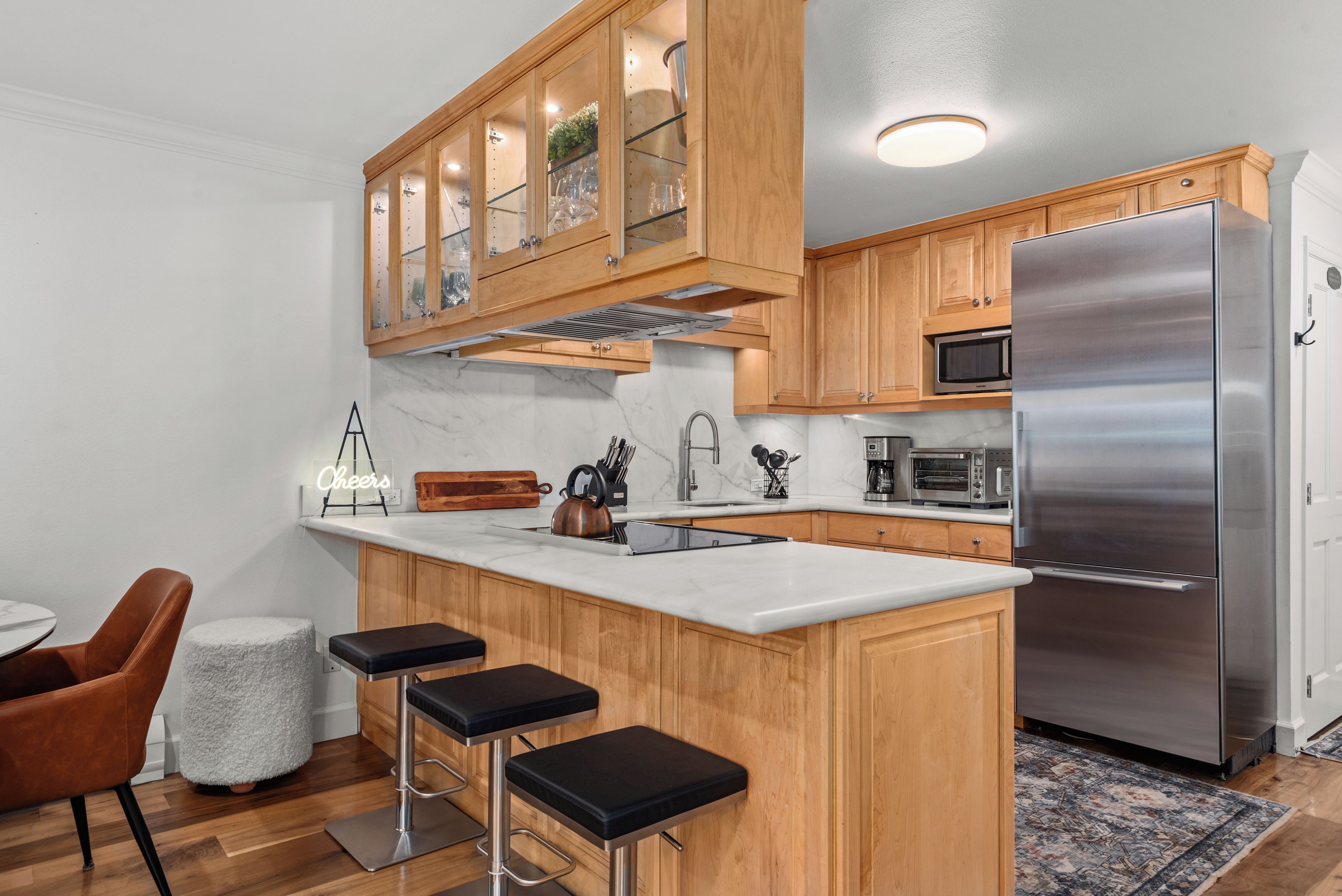A modern kitchen with wooden cabinets, a stainless steel refrigerator, and a bar area with stools.