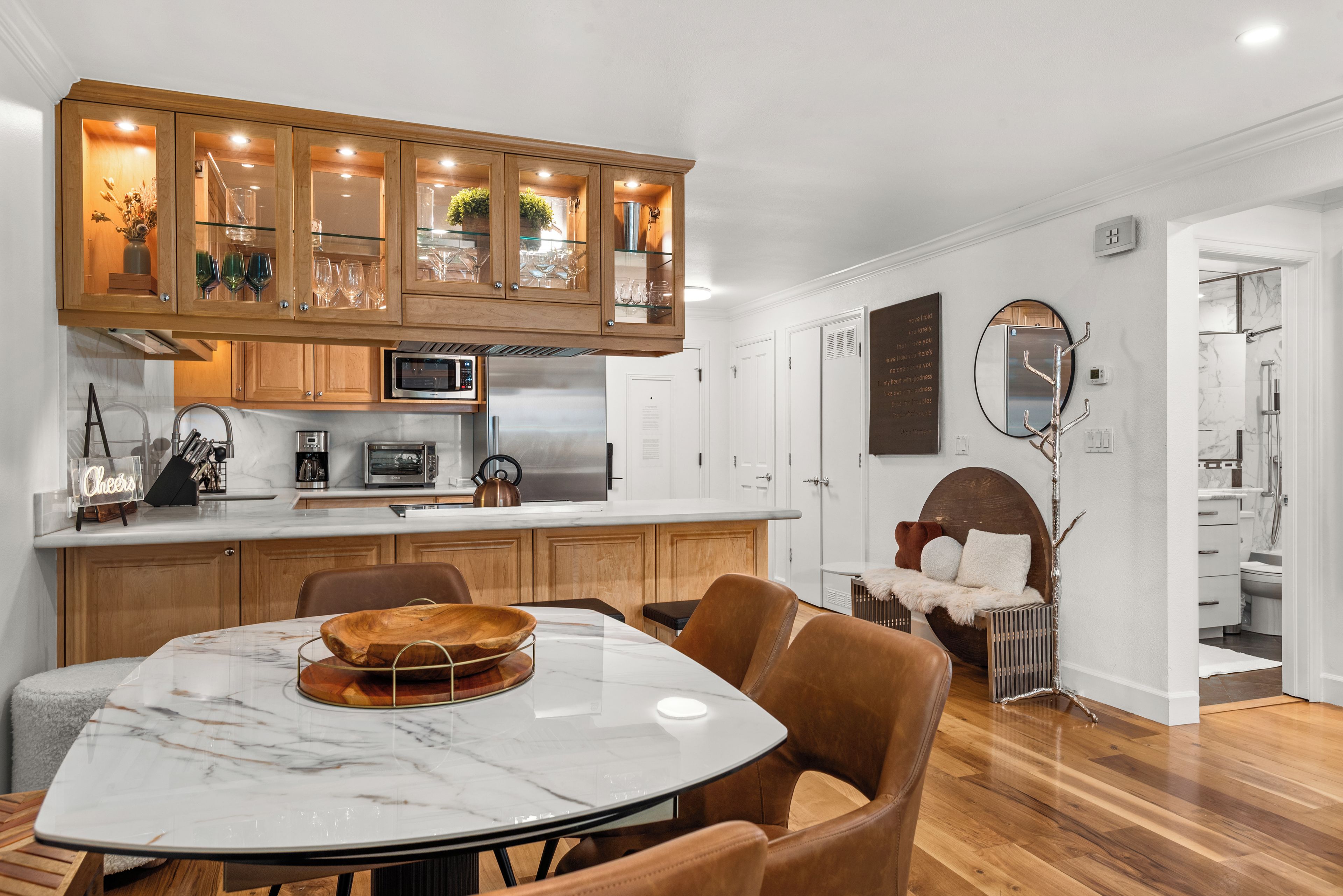 A modern kitchen with wooden cabinets, a built-in microwave, and a dining area with a marble table and leather chairs.