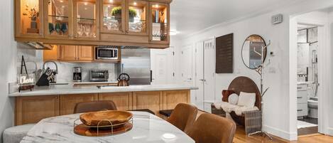 A modern kitchen with wooden cabinets, a built-in microwave, and a dining area with a marble table and leather chairs.