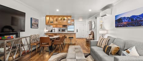 A modern living room with a grey sofa, wooden dining table, and a kitchen in the background.