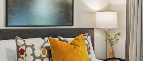 A hotel room with a bed, a painting, a lamp, and a curtain.