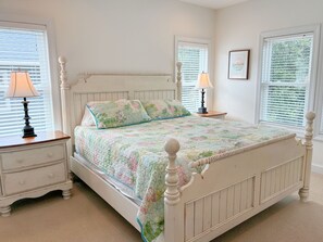 A bedroom with a white bed, two bedside tables with lamps, a dresser, and a framed picture on the wall. - Kookoolamonga!: Oceanside, Pool, Hot Tub, Elevator, Game Room (Nags Head)
