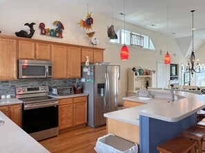 A modern kitchen with stainless steel appliances, wooden cabinets, and a large island with seating. - Kookoolamonga!: Oceanside, Pool, Hot Tub, Elevator, Game Room (Nags Head)