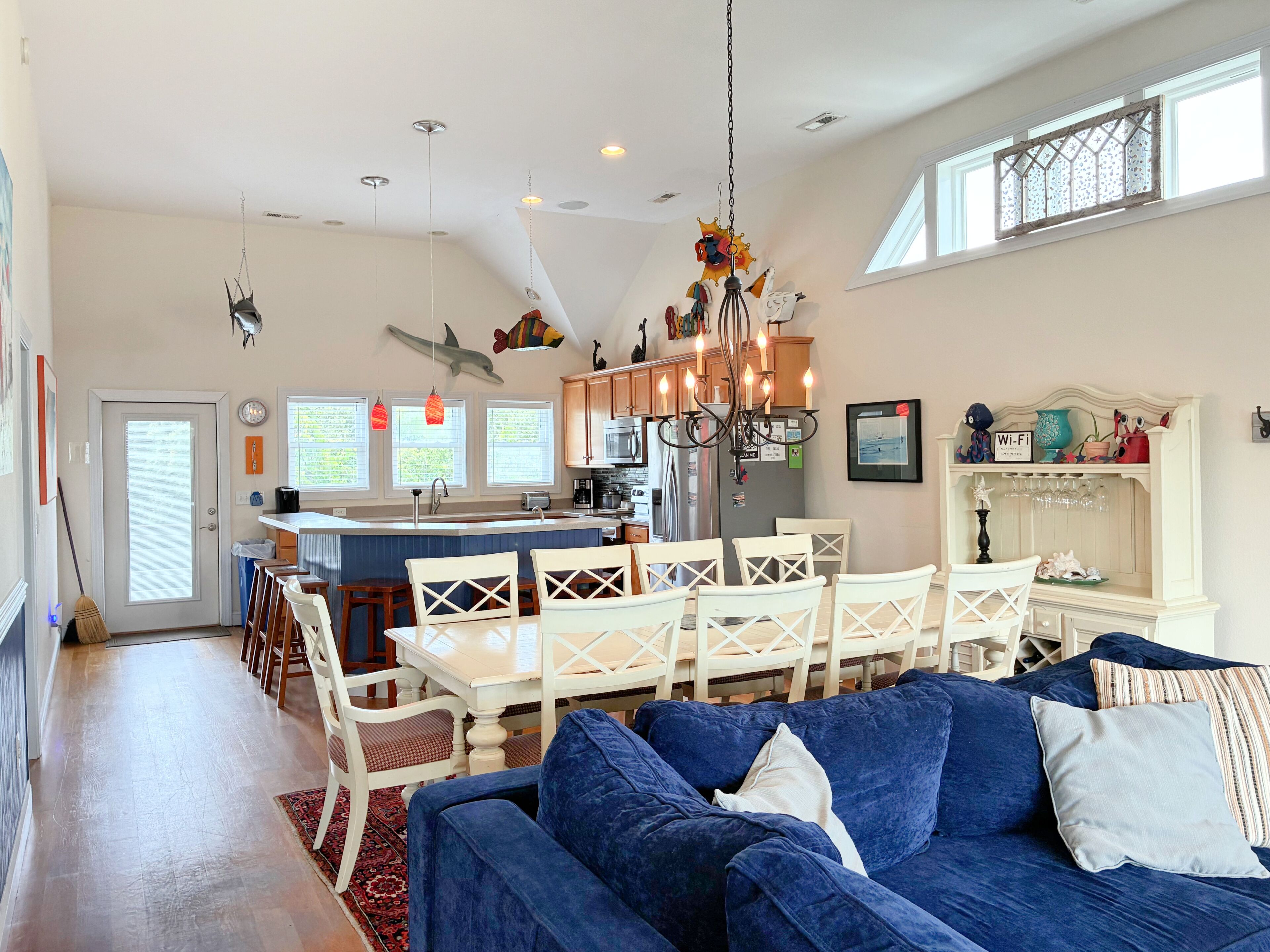 A spacious kitchen with a central island, white dining chairs, and a blue sofa in a bright living area with large windows.