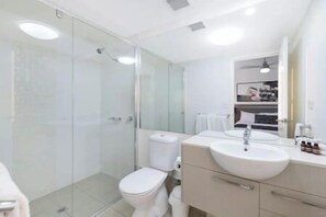 A modern bathroom with a glass shower enclosure, a white toilet, and a sink with a mirror above it. - Kensington Place Retreat - Studio (Townsville City)