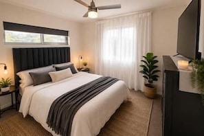 A bedroom with a bed, bedside tables, a ceiling fan, a TV, and a window with curtains. - Kensington Place Retreat - Studio (Townsville City)