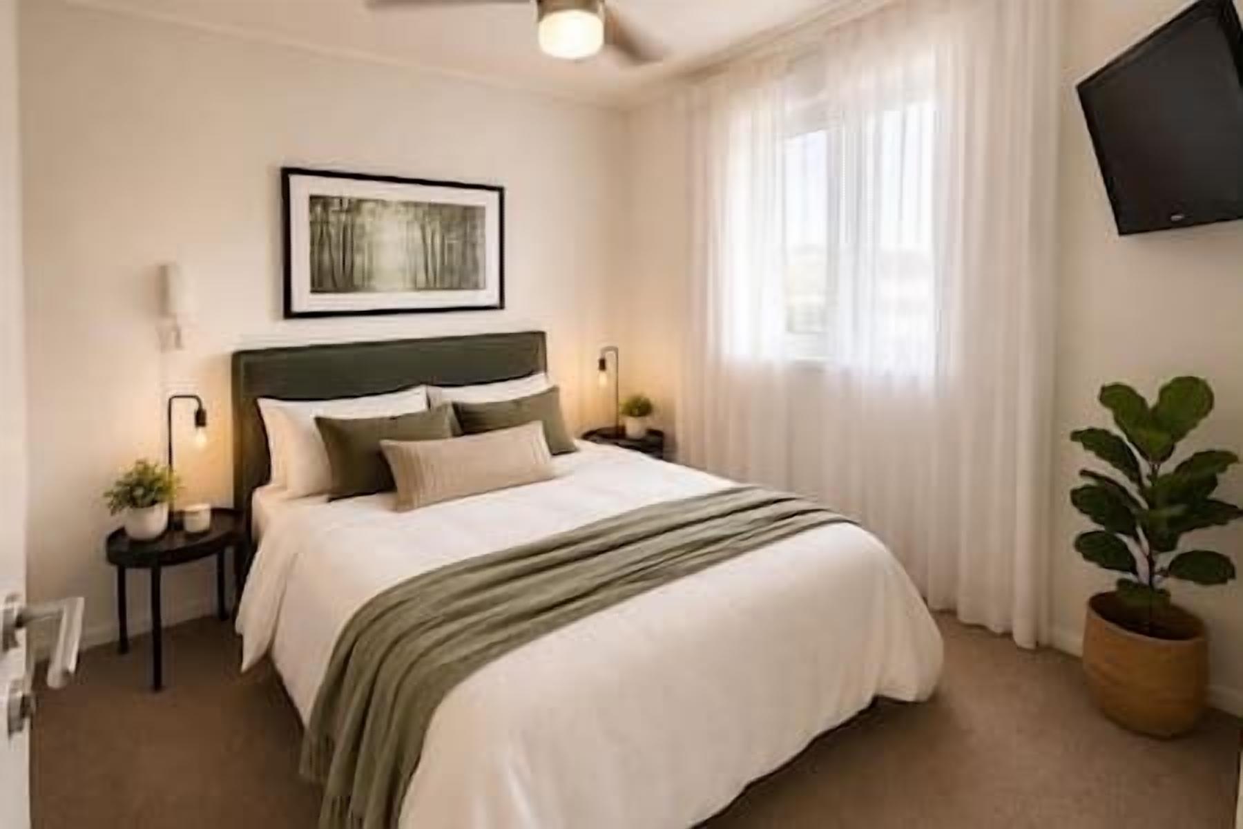 A neatly arranged bedroom with a bed, bedside tables, a wall-mounted TV, and a window with curtains.