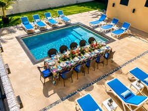 Ein Essbereich am Pool mit einem für sechs Personen gedeckten Tisch, umgeben von Liegestühlen.