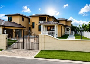 A multi-story house with a gated entrance, a well-maintained lawn, and a clear sky.