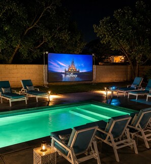 A swimming pool area with lounge chairs and a large screen displaying the Disney logo.