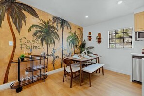 A dining area with a mural of palm trees and the text 'Casa Palma.' There is a dining table with chairs, a wine rack, and a refrigerator. - Casa Palma | Pool | Outdoor Fun | Near Beaches (Fort Lauderdale)