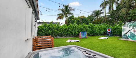 A backyard with a hot tub, a wooden fence, a target game, and a mural.