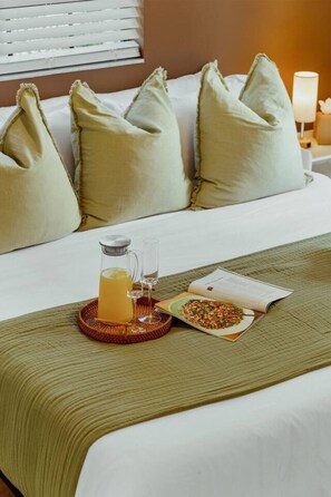 A neatly made bed with pillows, a glass of orange juice, a plate of food, and a book on a bedside table. - Casa Palma | Pool | Outdoor Fun | Near Beaches (Fort Lauderdale)