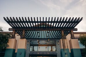 Ein Gebäudeeingang mit einer Holz-Pergola, einer gemusterten Wand und einem kleinen Balkon.