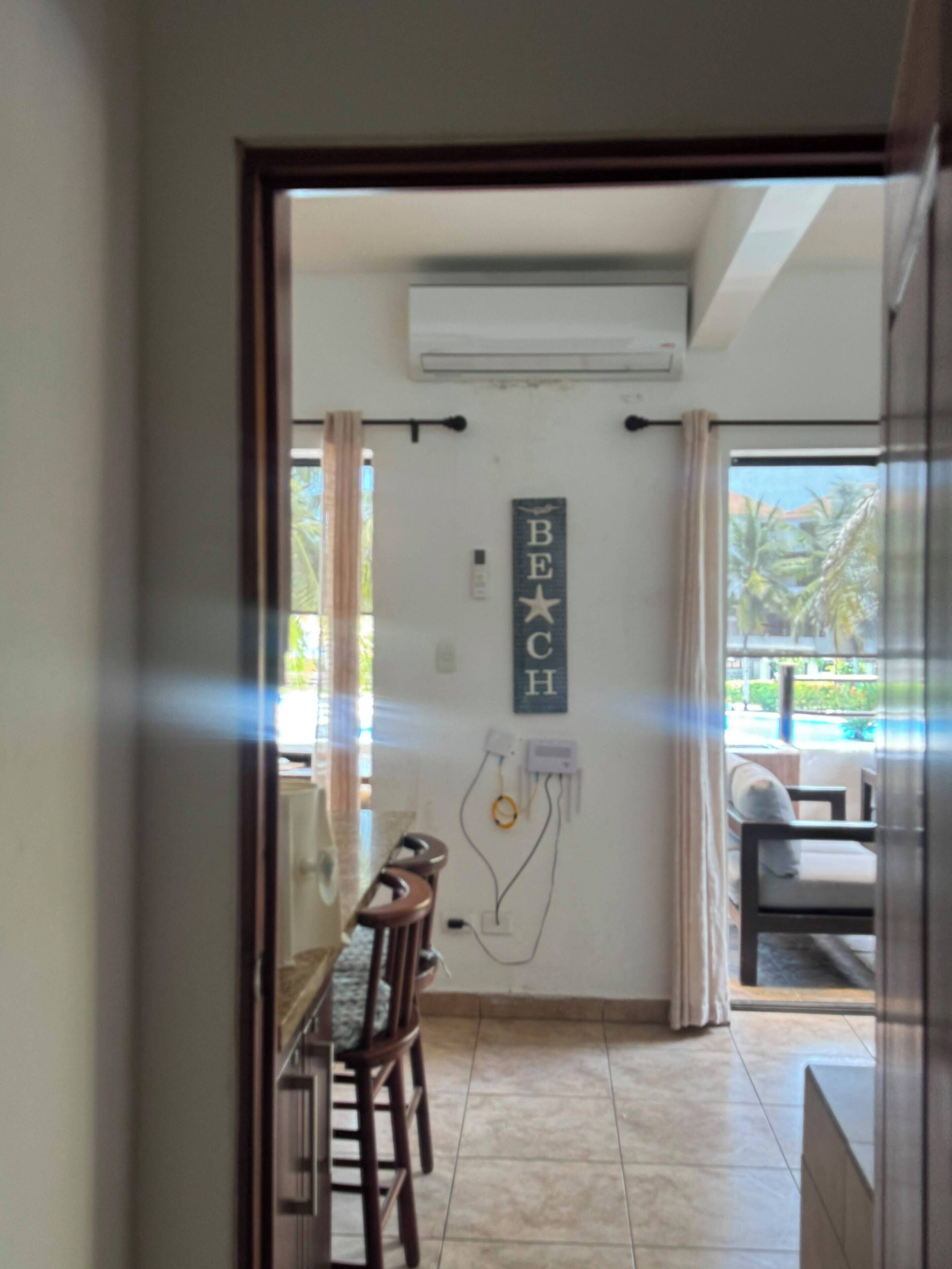 Un pasillo que conduce a un comedor con una mesa y sillas, un equipo de aire acondicionado instalado en la pared y un cartel que dice 'BEACH'.