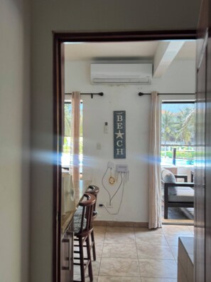 A hallway leading to a dining area with a table and chairs, a wall-mounted air conditioning unit, and a sign that reads 'BEACH'.