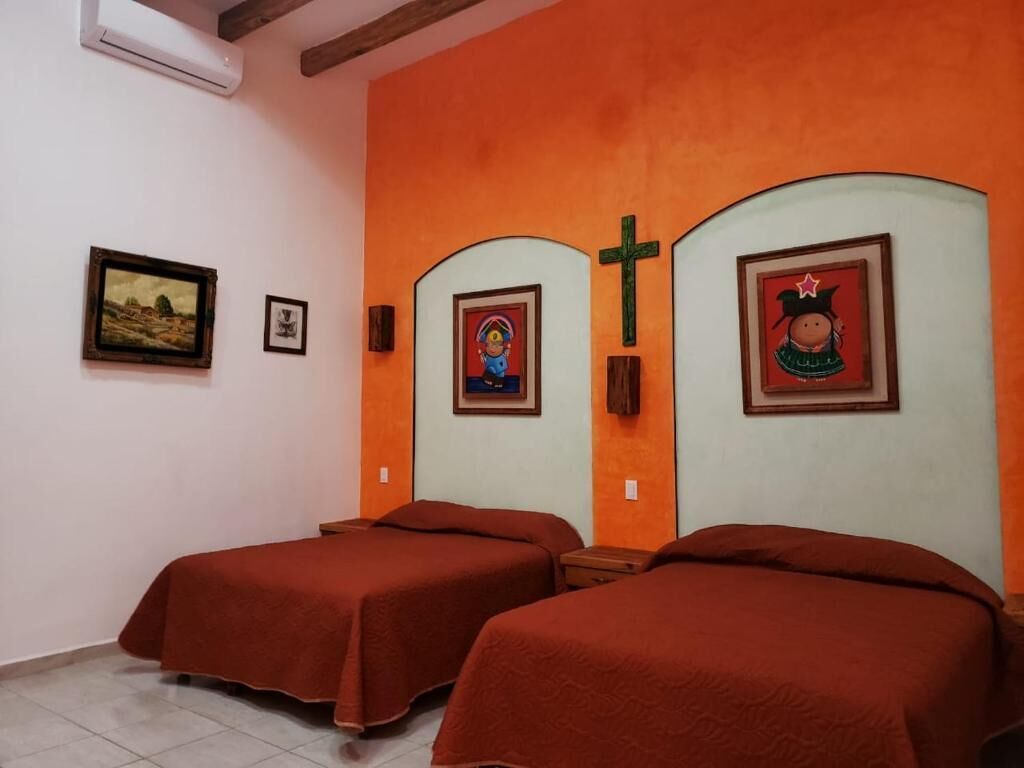 A room with two beds, a cross on the wall, and framed pictures.